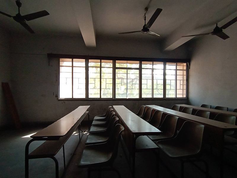 Empty lecture room with benches, ceiling fans and tall windows