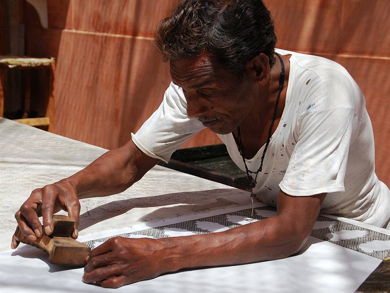 An artisan pressing a carved wooden block onto white cotton fabric